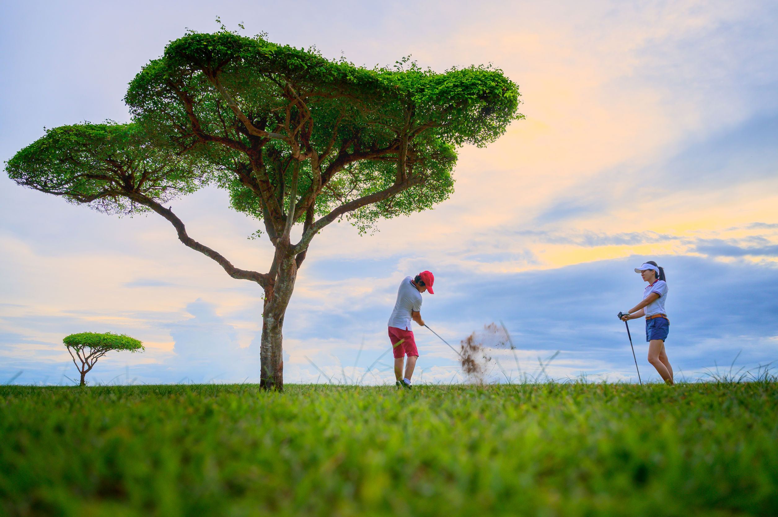 Two golfers playing on a course at sunset