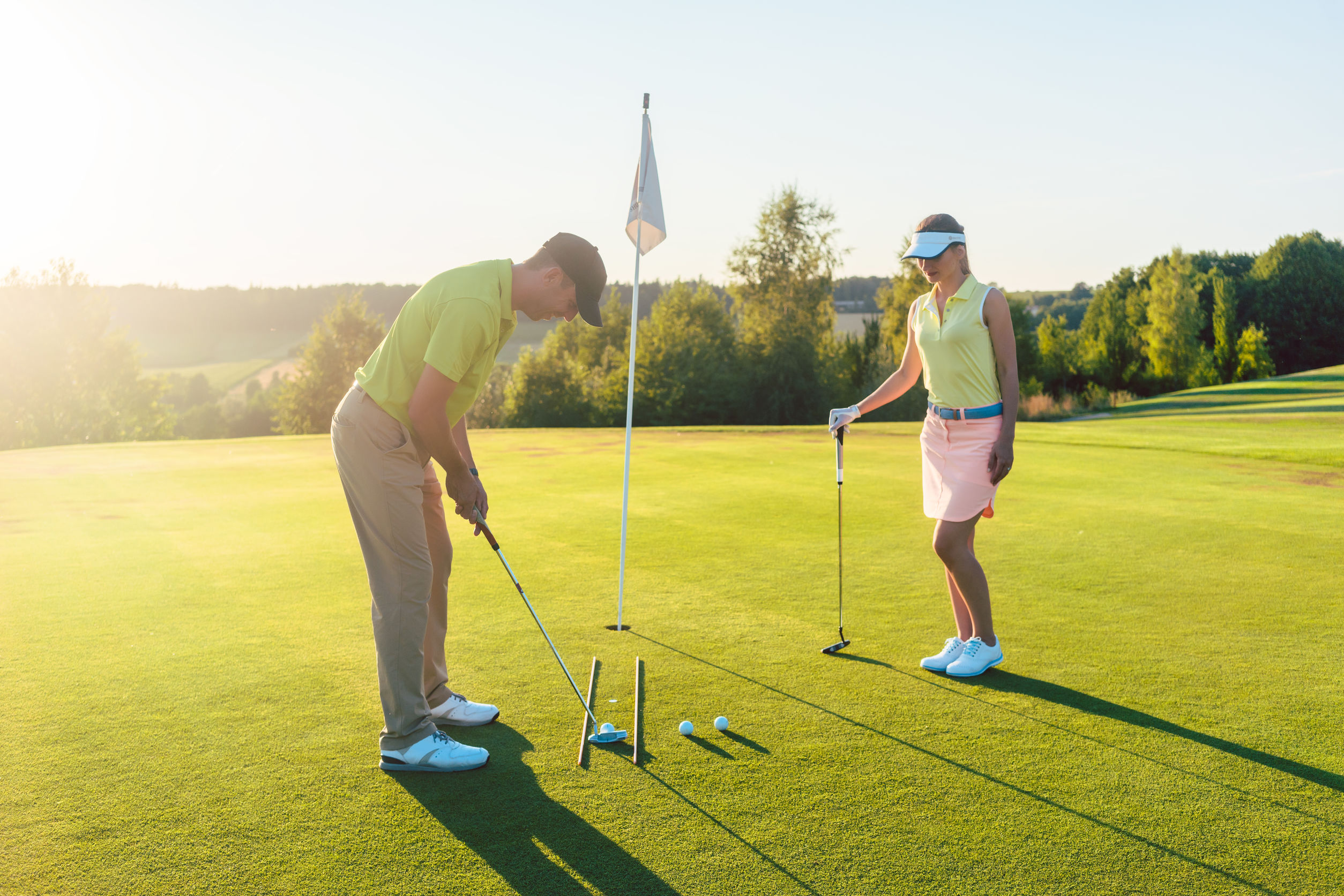 Two golfers on a putting green at sunset